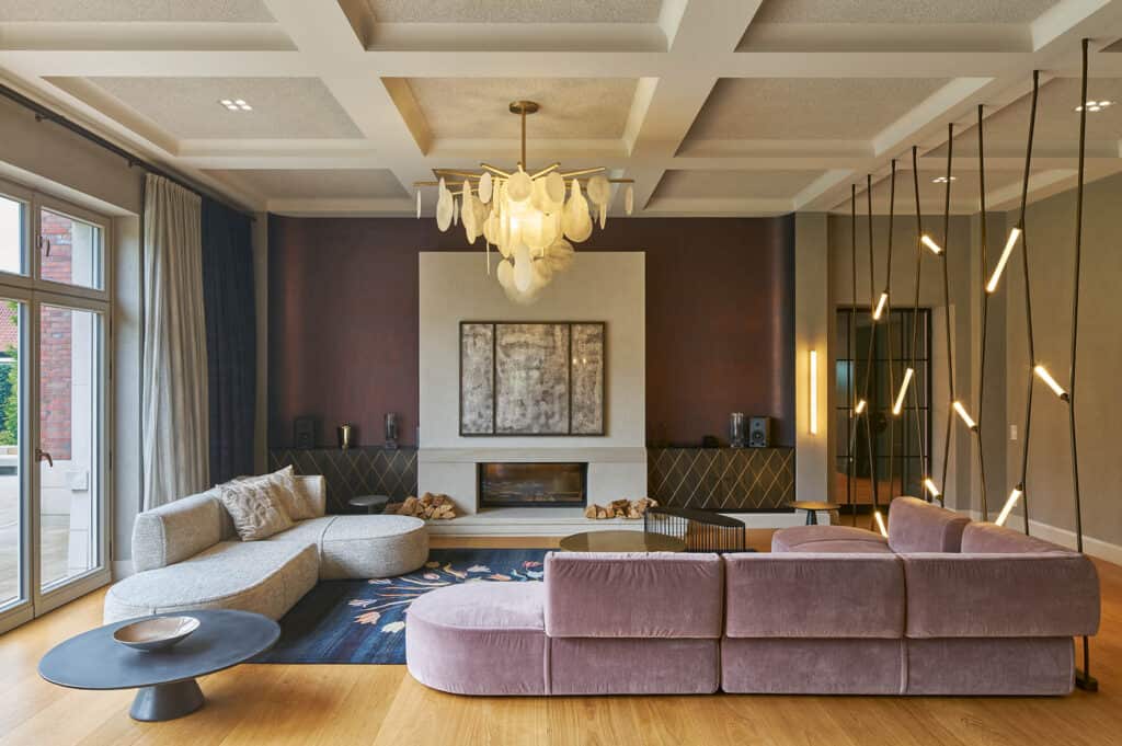 großes Wohnzimmer mit einem rosa Sofa, modernen Lampen und einem weißen Kamin