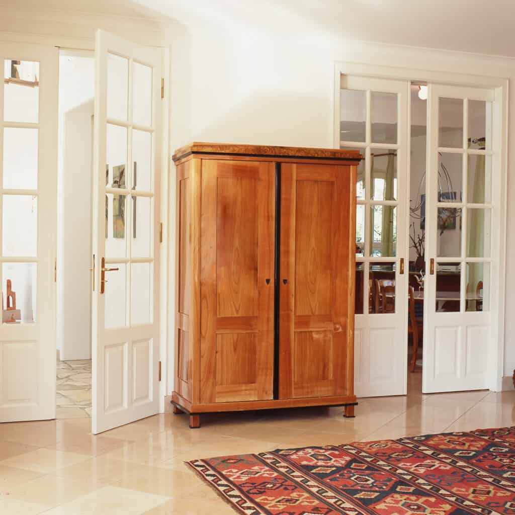braune Holzkommode in einem hellen Raum mit weißen offenen Türen